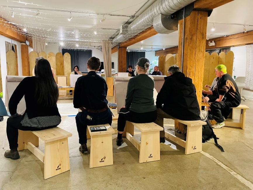 Artists at a NOOD life drawing session, seated on wooden benches in a timber-beamed studio.